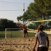Persone giocano a beach volley su un campo sabbioso con reti e alberi intorno.