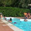 Piscina con bambini che nuotano e adulti seduti sotto ombrelloni.