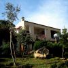 Casa mediterranea con balconi, circondata da alberi e arbusti.
