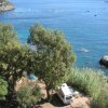 Vista dall'alto di un campeggio su una costa rocciosa con alberi e mare.