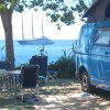 Un furgone blu accanto al mare con un'imbarcazione a vela in lontananza.