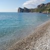 Spiaggia di ciottoli con mare limpido e scogliere sullo sfondo.