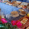 Buffet della colazione con cereali, dolci, frutta e uova esposto su tovaglie blu.