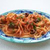 Piatto di spaghetti con polpo e olive nere in salsa rossa, guarnito con prezzemolo.