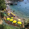 Spiaggia con ombrelloni gialli, mare azzurro e barche al largo. Persone prendono il sole e nuotano.