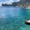 Costa con acque turchesi, un molo e colline verdi in lontananza.