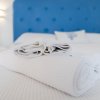 Letto con testiera blu e asciugamani bianchi piegati sopra. Sfondo bianco e luminoso.