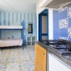 Cucina con fornelli, tavolo con sedie e letti a castello, pareti azzurre e piastrelle colorate.