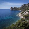 Vista aerea di una costa rocciosa con case e mare blu profondo.