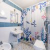 Bagno con piastrelle blu e bianche, doccia con tenda colorata a tema marino e lavabo con specchio.