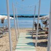 Spiaggia con ombrelloni e lettini, passerella verso il mare.