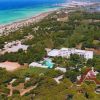 Veduta aerea di un hotel circondato da alberi vicino a una lunga spiaggia di sabbia e mare azzurro.