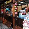 Bancone di uno stabilimento balneare, donna ordina una bevanda, luci calde e bevande esposte.