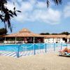 Piscina con sdraio e un grande gazebo in legno, circondata da alberi e cielo blu.