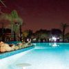Piscina illuminata di notte, con palme e rocce decorative lungo il bordo.