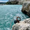 Vista di un paese su una scogliera, mare turchese e un anello d'ormeggio in primo piano.