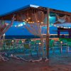 Bar sulla spiaggia illuminato di sera, con sedie verdi.