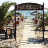 Ingresso a una spiaggia con ombrelloni e palme.