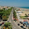 Viale alberato lungo la costa con spiaggia e ombrelloni.