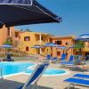 Piscina circondata da lettini e ombrelloni blu, edifici colorati sullo sfondo.