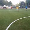Giocatori corrono su un campo di calcio in erba sintetica.