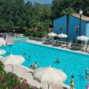Piscina all'aperto con sdraio e ombrelloni bianchi, circondata da vegetazione e un edificio blu.