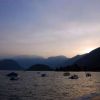 Lago al tramonto con barche ormeggiate e montagne sullo sfondo.