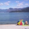 Una spiaggia con un ombrellone colorato e un lago circondato da montagne.