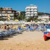 Spiaggia con ombrelloni e lettini, palazzi sullo sfondo.
