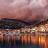 Un villaggio costiero riflesso in acqua, con cielo nuvoloso e montagne sullo sfondo.