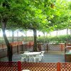 Un cortile con tavoli e sedie bianche, circondato da una staccionata e alberi frondosi.