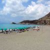 Spiaggia con lettini e ombrelloni, mare azzurro e colline sullo sfondo.