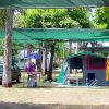 Una tenda verde con ombrellone e sedie sotto alberi ombreggiati vicino a un'auto.