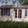Una piccola casa beige con tetto rosso, finestre con persiane blu e una porta centrale vetrata.