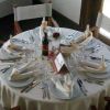 Tavola rotonda apparecchiata con piatti, posate, bicchieri, tovaglioli e una bottiglia di vino.