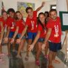 Un gruppo di persone sorride con magliette rosse e jeans corti, posando in un interno luminoso.
