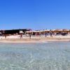 Spiaggia affollata con ombrelloni colorati e persone in acqua sotto un cielo blu.