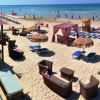Spiaggia con lettini in vimini, ombrelloni di paglia e una struttura rosa vicino al mare.