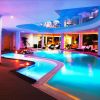Piscina interna con illuminazione colorata, lettini neri e ampie finestre con piante.