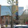 Edificio moderno con facciata in vetro e una scultura alta al centro, circondato da alberi.