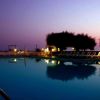Piscina illuminata al tramonto con sdraio allineate e alberi sullo sfondo.