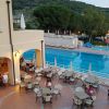 Piscina all'aperto con tavolini, alberi sullo sfondo.