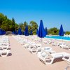 Piscina con lettini bianchi e ombrelloni blu, cielo sereno.