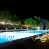 Piscina illuminata di notte, circondata da sdraio bianche e ombrelloni blu.