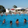Persone in cerchio in una piscina all'aperto con ombrelloni e un edificio bianco dietro.
