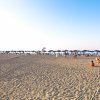 Spiaggia sabbiosa con ombrelloni blu e bagnanti sotto un cielo limpido.