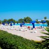 Piscina con sedie a sdraio bianche, ombrelloni blu e vegetazione verde intorno.