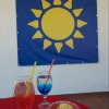Tavolo con cocktail colorati e patatine. Sfondo con un drappo blu e sole giallo.