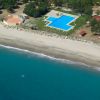 Piscina a forma irregolare vicino alla spiaggia sabbiosa con mare blu.
