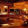 Bar all'aperto con tavoli, sedie e ombrelloni illuminati da luci soffuse.